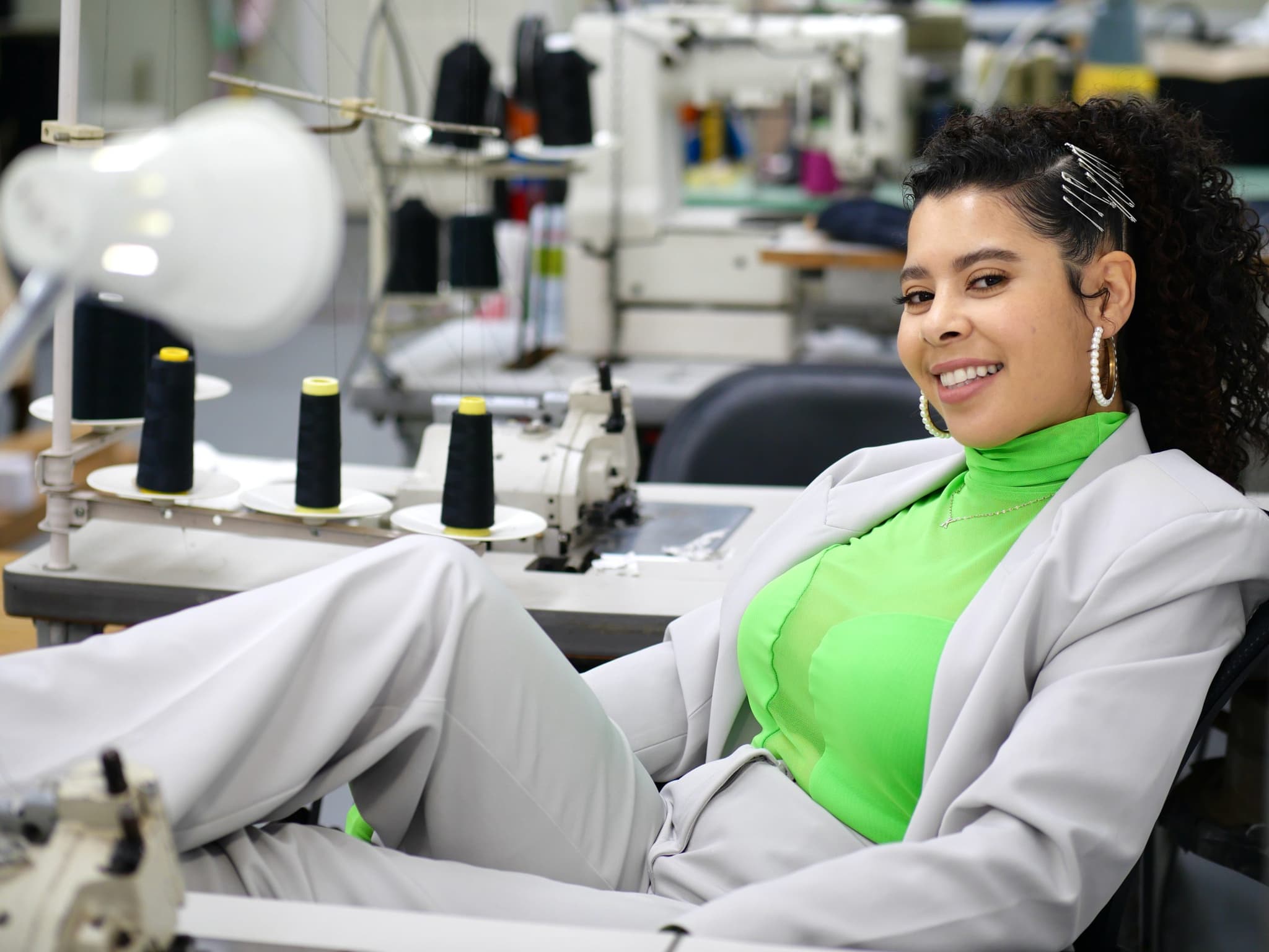 Karina Cardona at her sewing machine in the studio, in a pale grey suit.