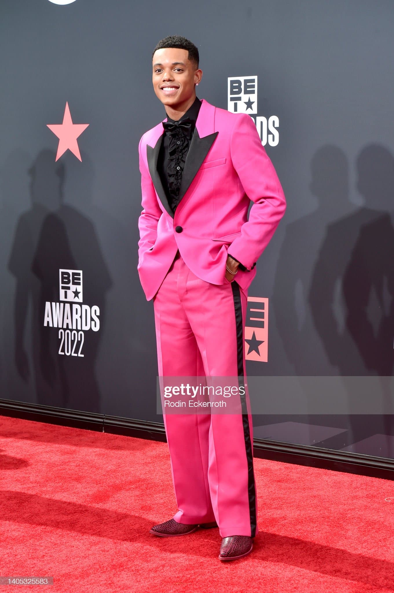 Hot pink tuxedo with black satin peak lapels and a matching trouser stripe, worn with a ruffled black shirt on the red carpet.
