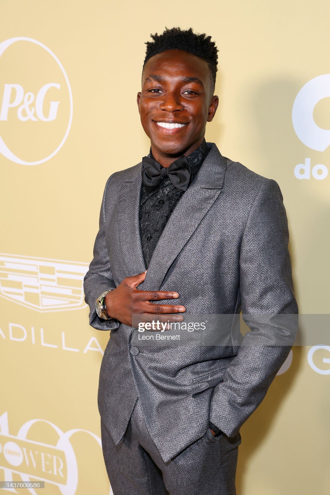 Charcoal textured tuxedo with peak lapels and a black bow tie, worn over a patterned black shirt on a step and repeat.