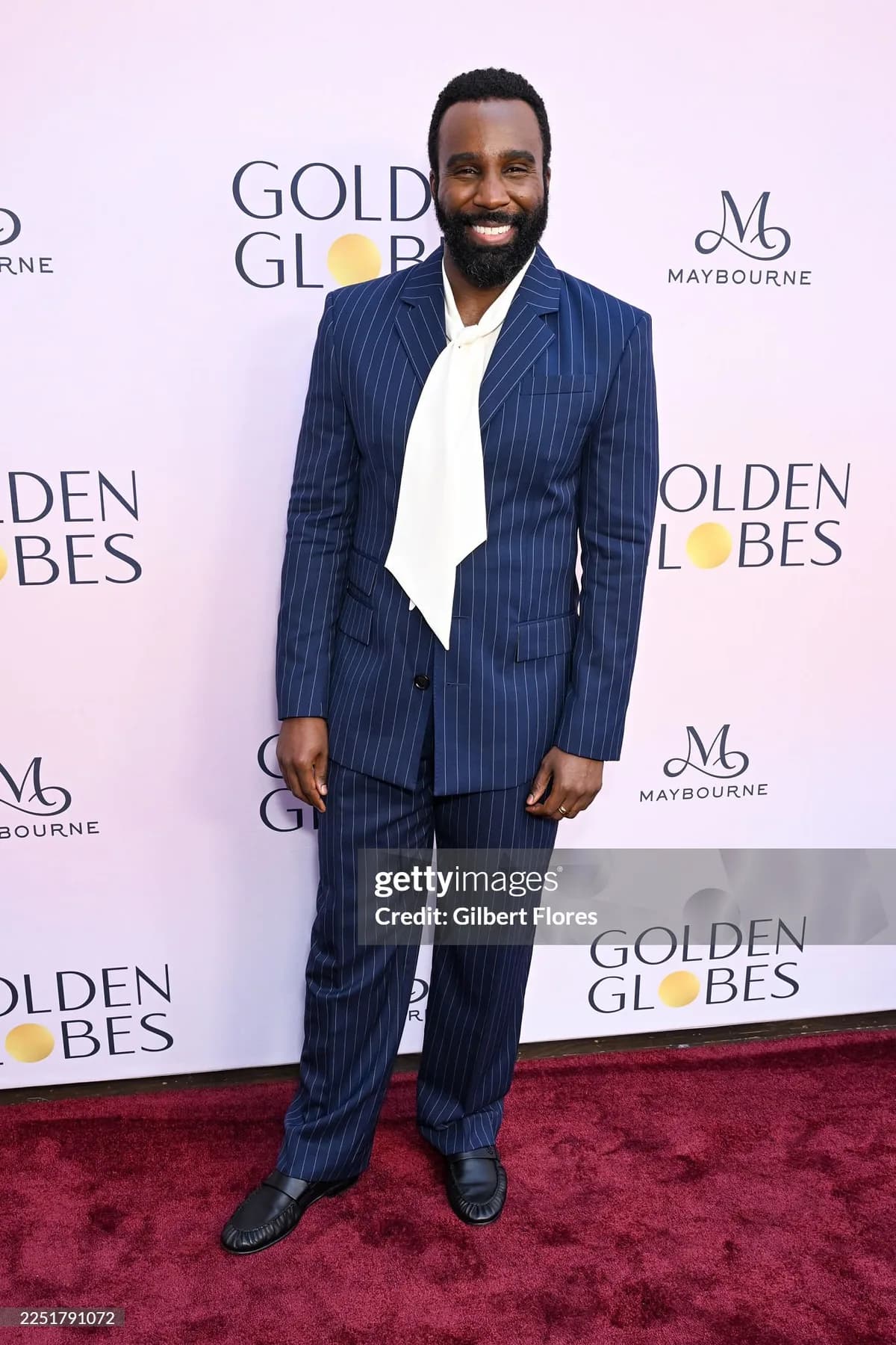 Full length navy pinstripe suit with a white cravat and black loafers on the Golden Globes red carpet.