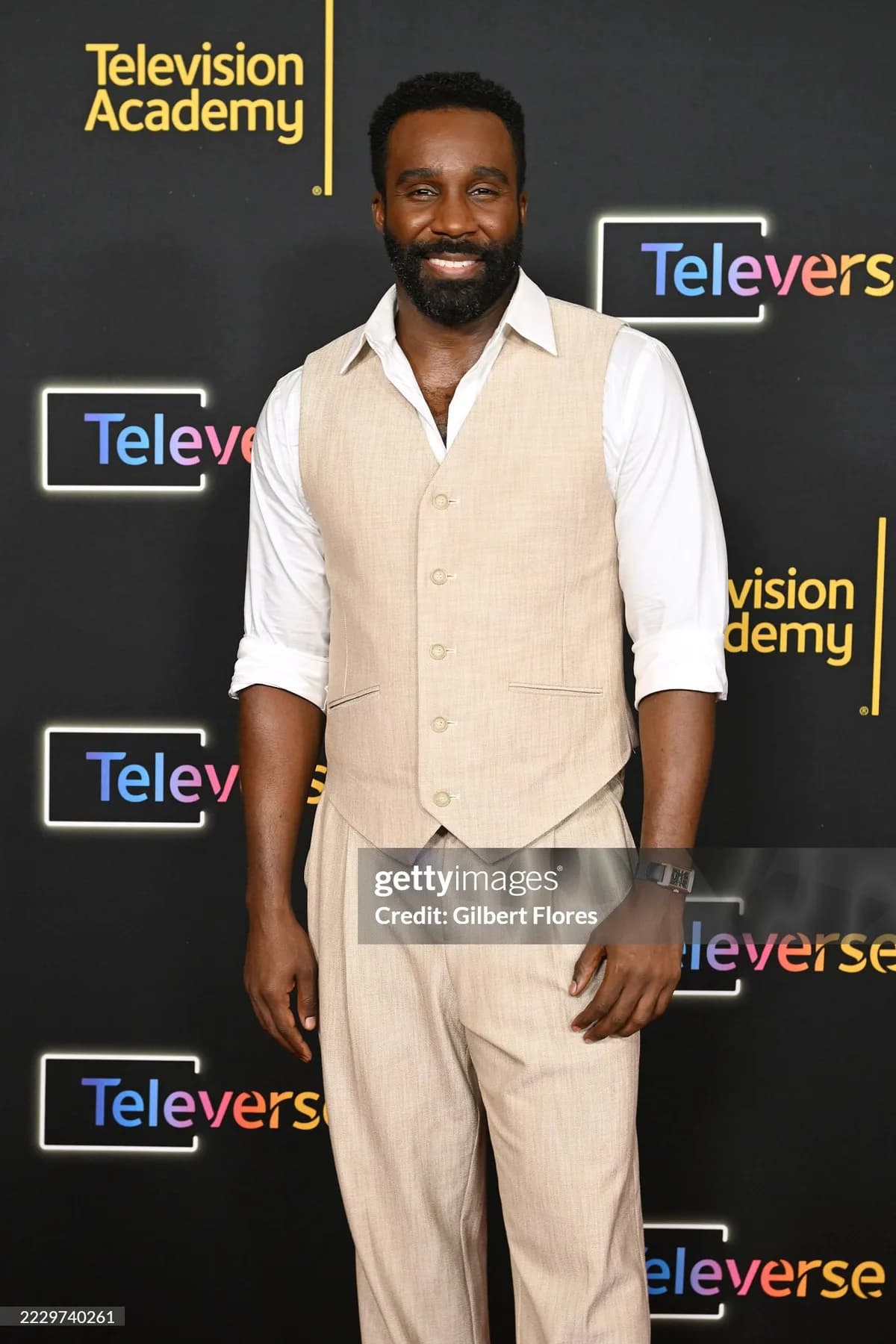 Sand linen waistcoat and matching trousers worn with a white shirt, sleeves rolled, on a dark press wall.