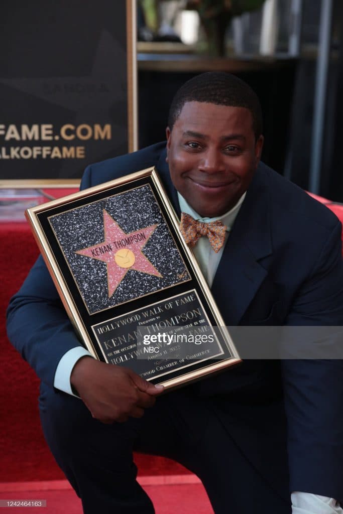 A guest in a navy suit and patterned bow tie holding a Walk of Fame plaque.